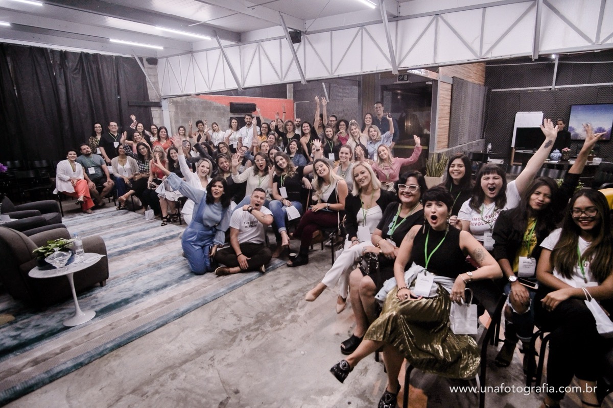 mais de cinquenta pessoas reunidas numa edição do café com branding, com os braços levantados