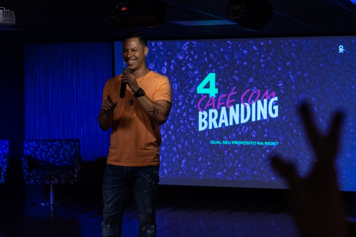 kerk de camisa laranja numa edição do café com branding, com o telão do evento ao fundo